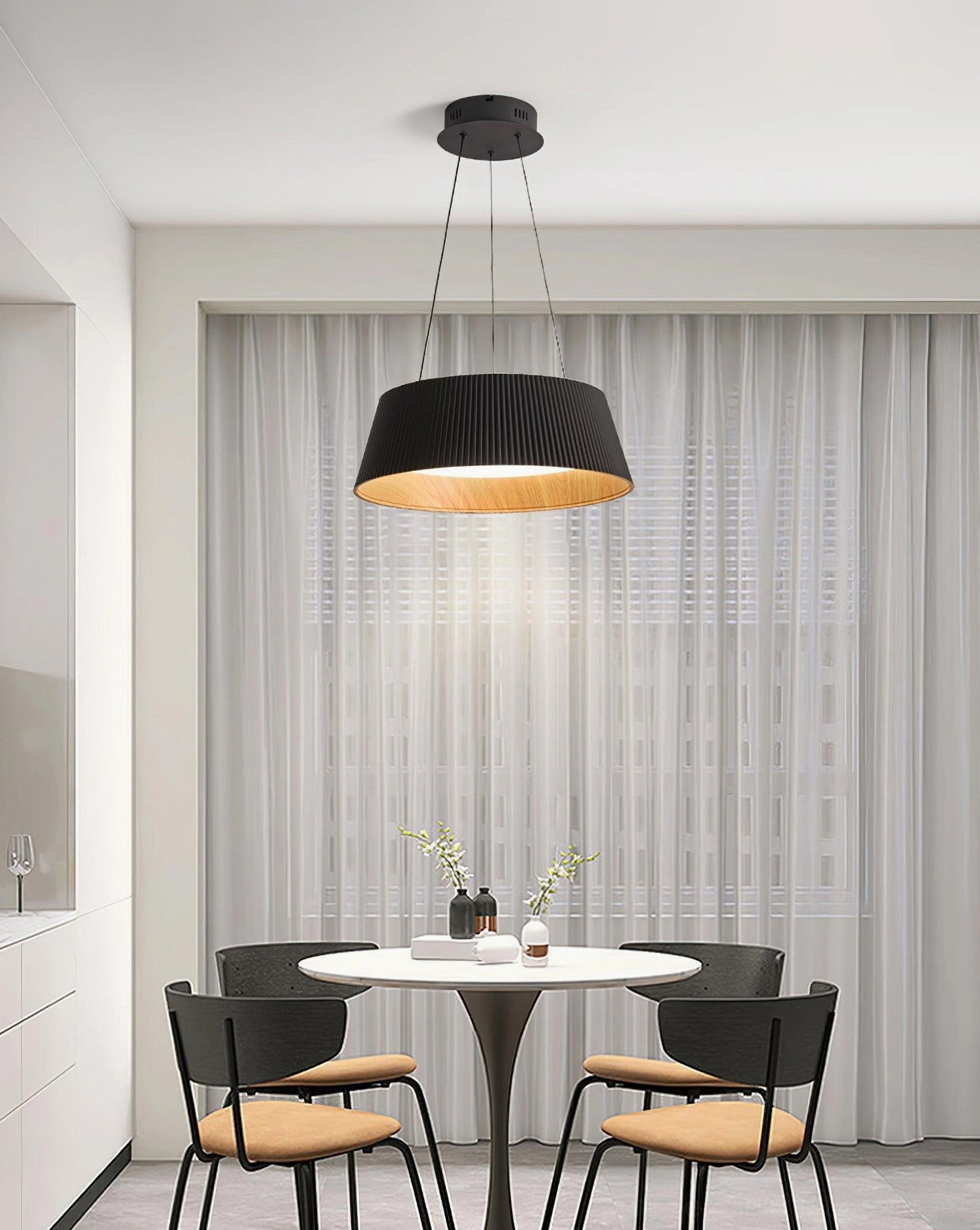 Black Delta drum pendant light above round dining table in modern apartment, minimalist interior design