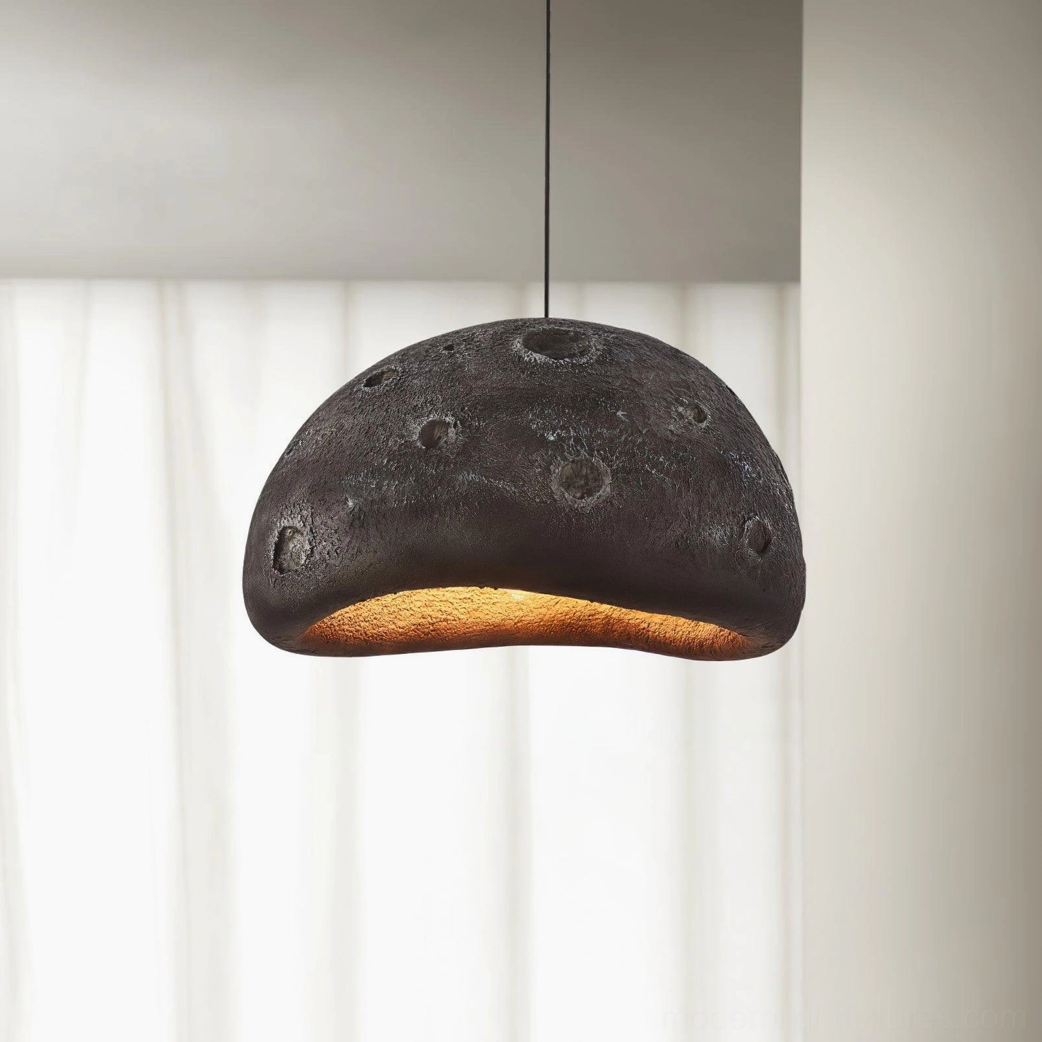 Black meteorite crater pendant light with matte crater-textured dome and warm underglow on minimalist backdrop