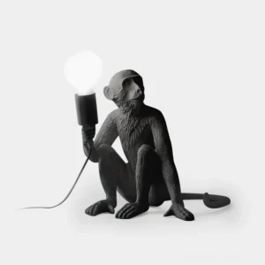 Black matte resin monkey table lamp in sitting pose with exposed bulb, front flat studio view