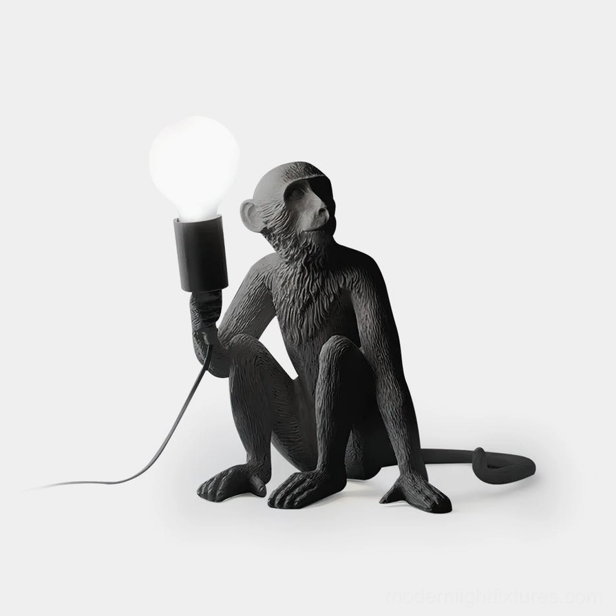 Black matte resin monkey table lamp in sitting pose with exposed bulb, front flat studio view
