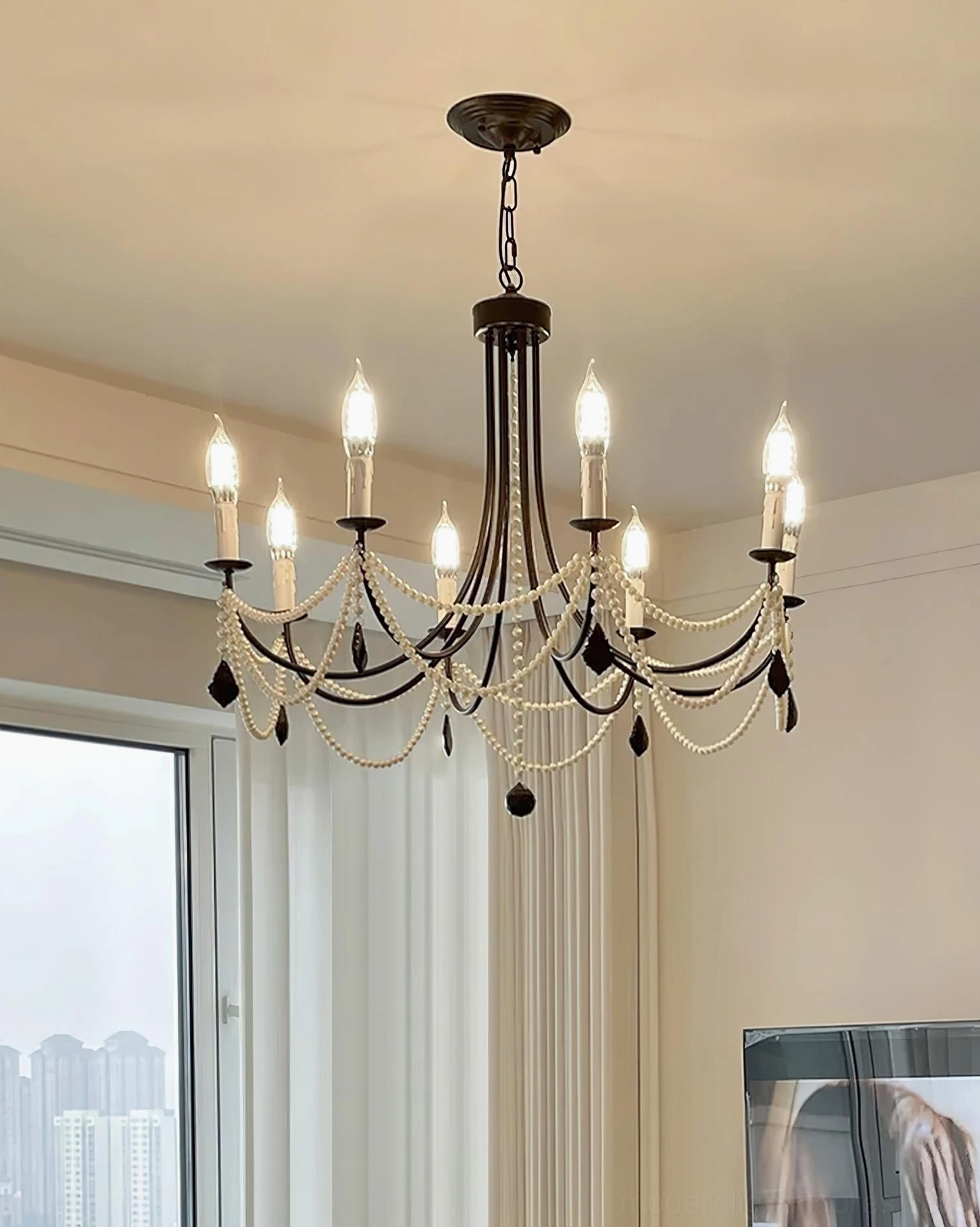 Matte black vintage chandelier with pearl beads and crystal drops in bright apartment with natural window light