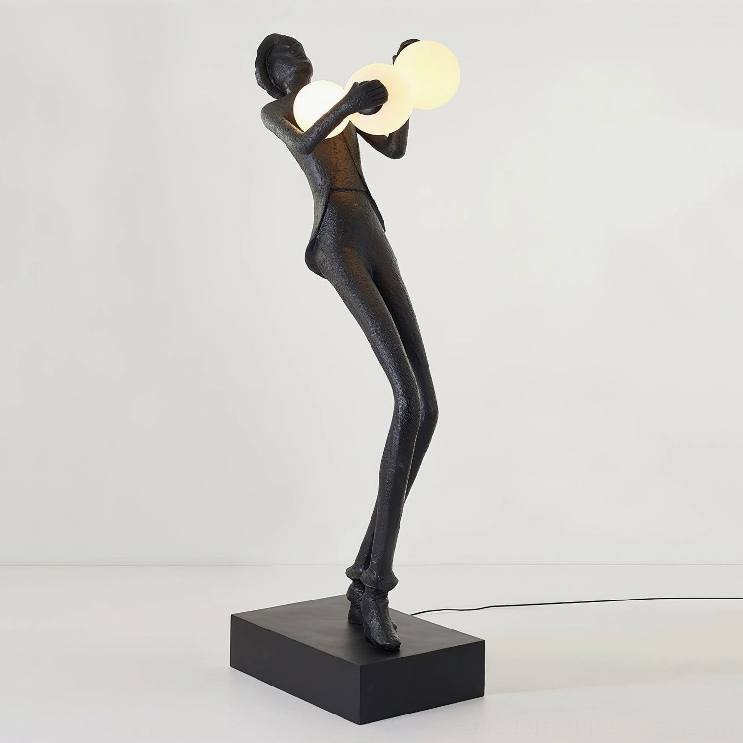 Black matte humanoid sculptural floor lamp with two frosted glass lights showing visible power cord on base, studio white background