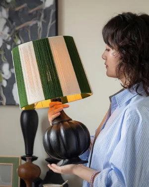 Black pumpkin base table lamp with striped shade, side close-up showing inner glow and craftsmanship detail