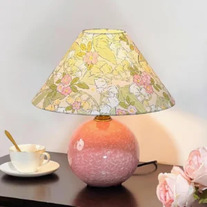 Bloomora table lamp with botanical fabric shade on dark wooden bedside table, styled with coffee cup and fresh roses