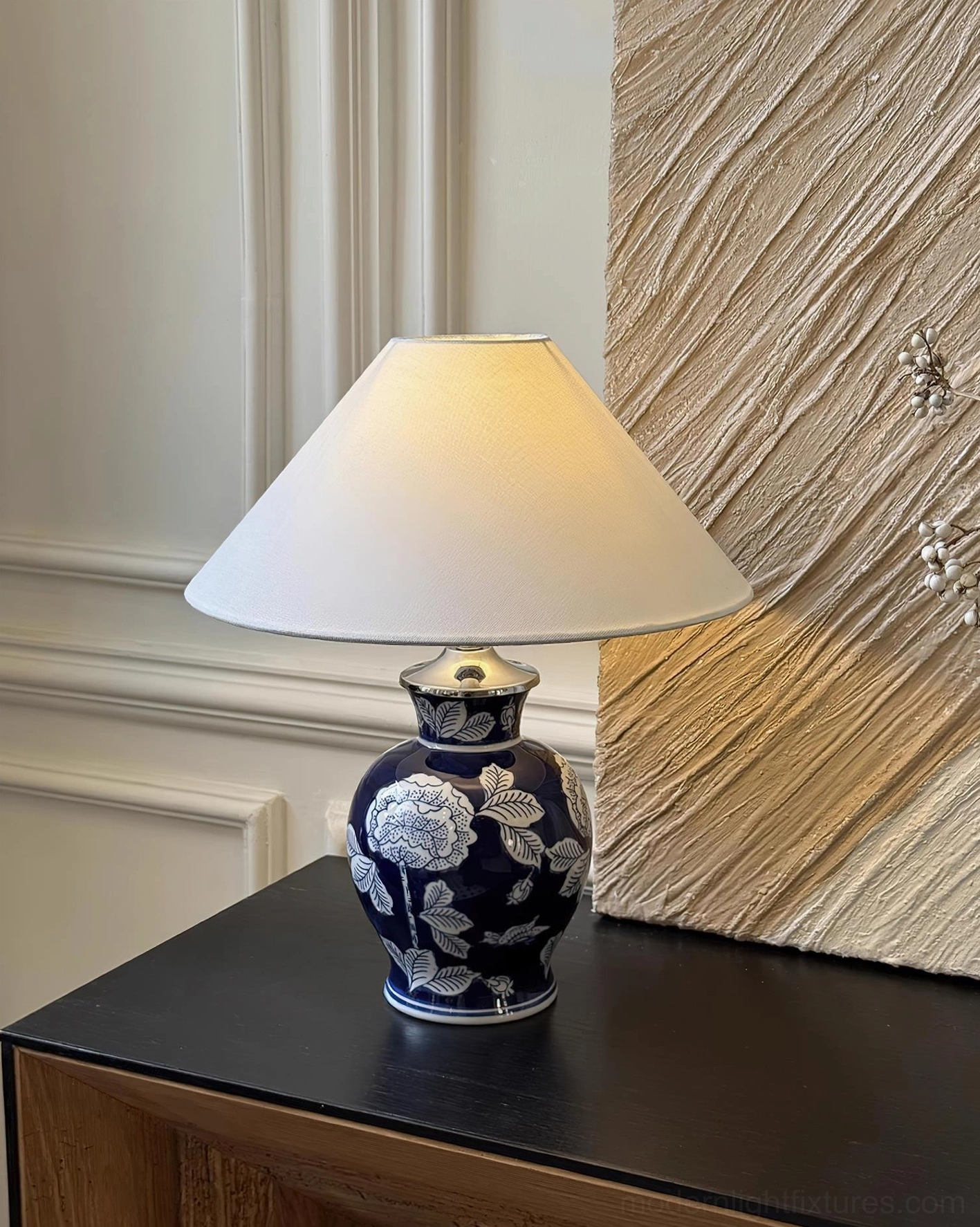 Dark blue ceramic table lamp with white floral motifs and fabric shade, displayed on luxury home side table with decor