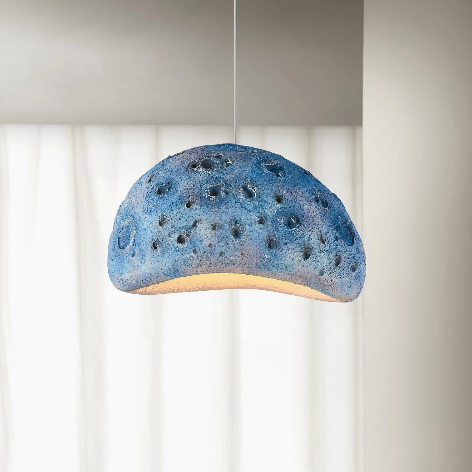 Blue meteorite crater pendant light with textured semi-spherical dome and downward warm glow in studio setting