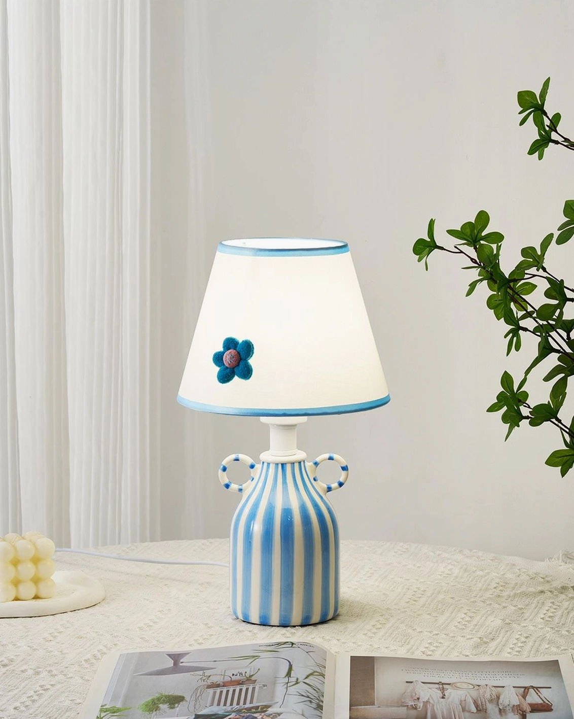 Mediterranean-inspired ceramic table lamp with striped base styled in bedroom with green plant accent