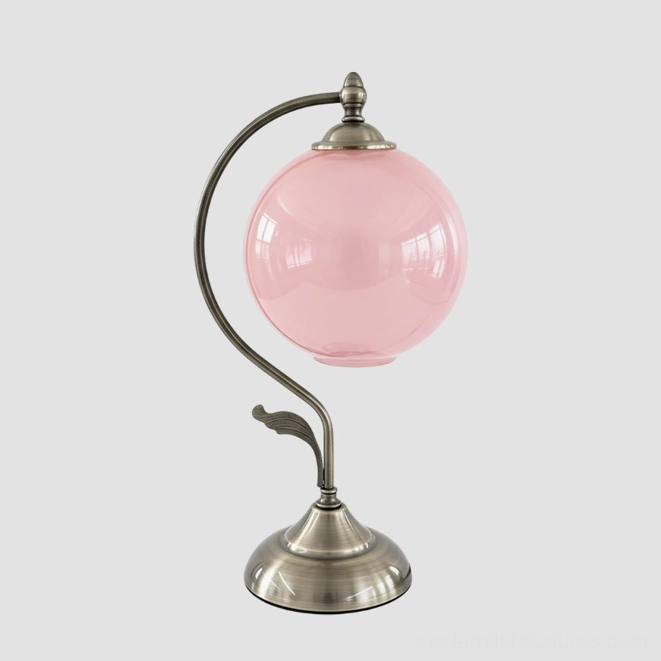 Blush pink frosted globe table lamp with elegantly arched brass support, romantic vintage-inspired color option for bedroom decor