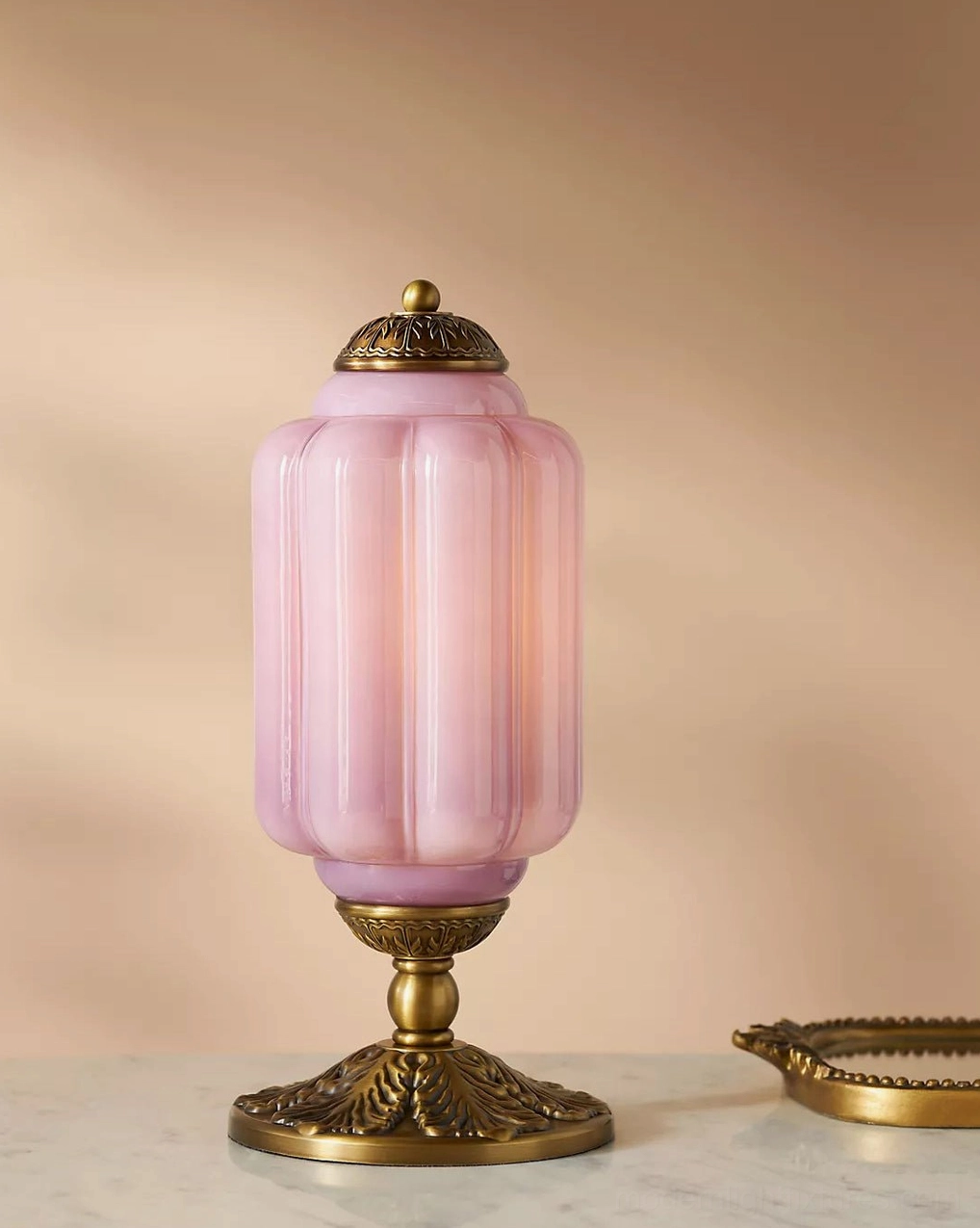 Blush pink fluted glass table lamp with bronze base on marble table with decorative gold tray