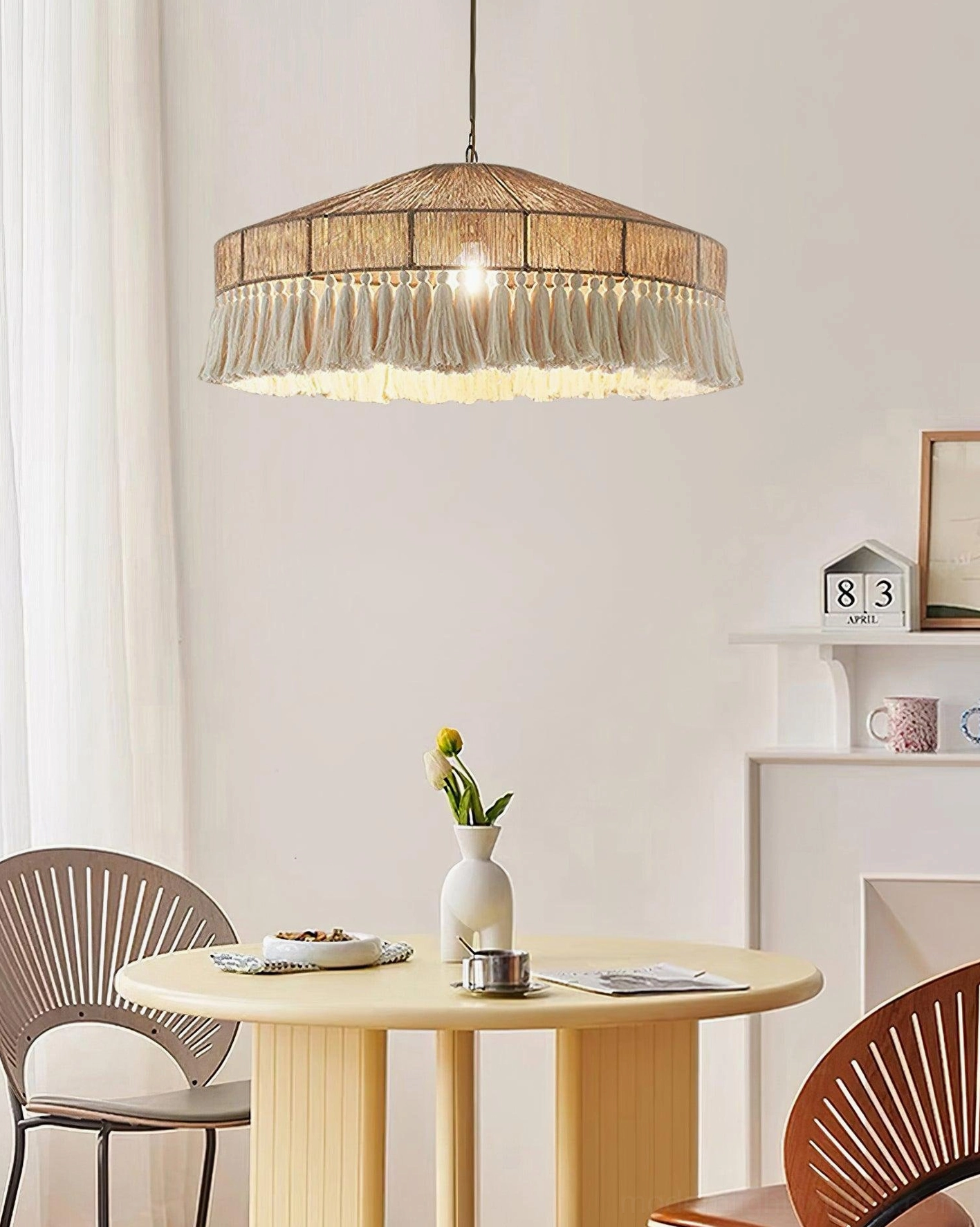 Handwoven bohemian fringe pendant lamp suspended over round wooden table in small dining space, warm neutral tones creating intimate boho dining area