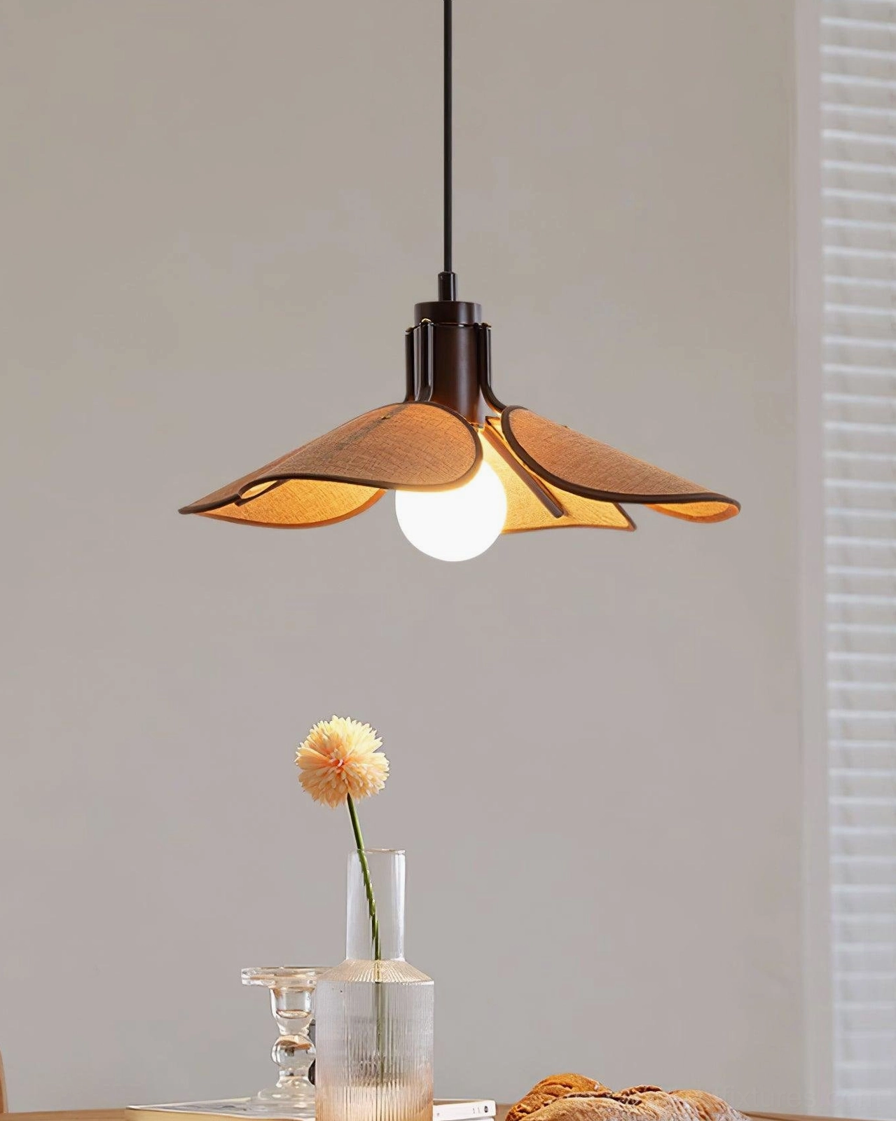 Boho rattan pendant light with exposed bulb over dining table, front angled view with warm lighting