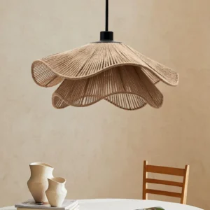 Boho straw hat hanging lamp illuminated above dining table in cozy rustic interior, showing warm ambient glow and textured woven shade