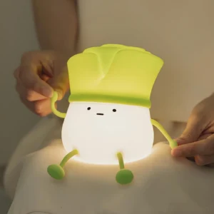 Hands holding soft silicone bok choy night light glowing warm white on bed