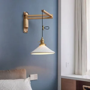 Swing arm wall sconce installed above bedroom bedside table with light oak wood frame and pleated off-white ceramic lampshade