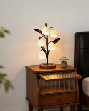 Botanical table lamp placed on vintage wooden nightstand with potted plant in bedroom setting