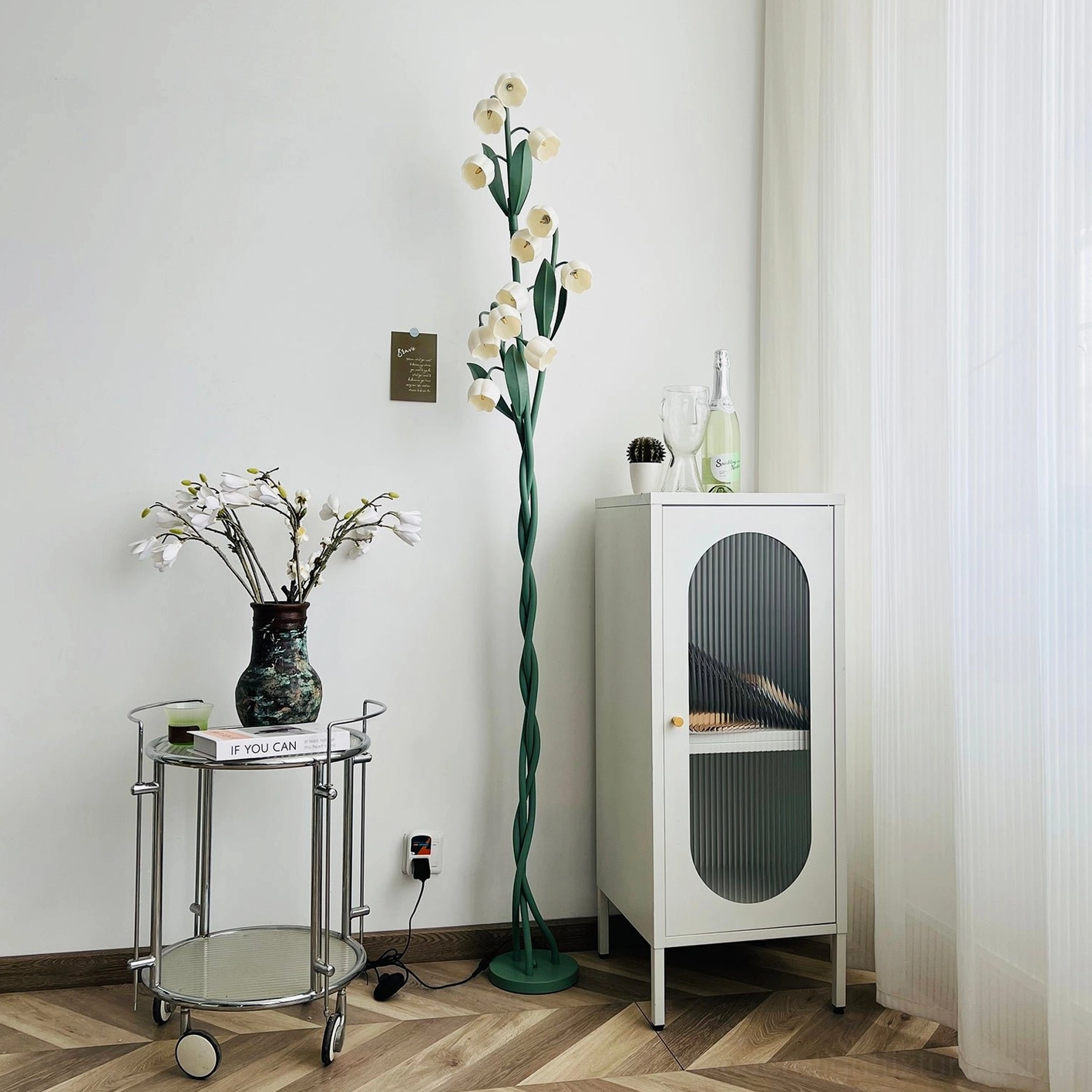 Modern botanical floor lamp in small living room corner with metal trolley cart and white storage cabinet, lifestyle interior design shot