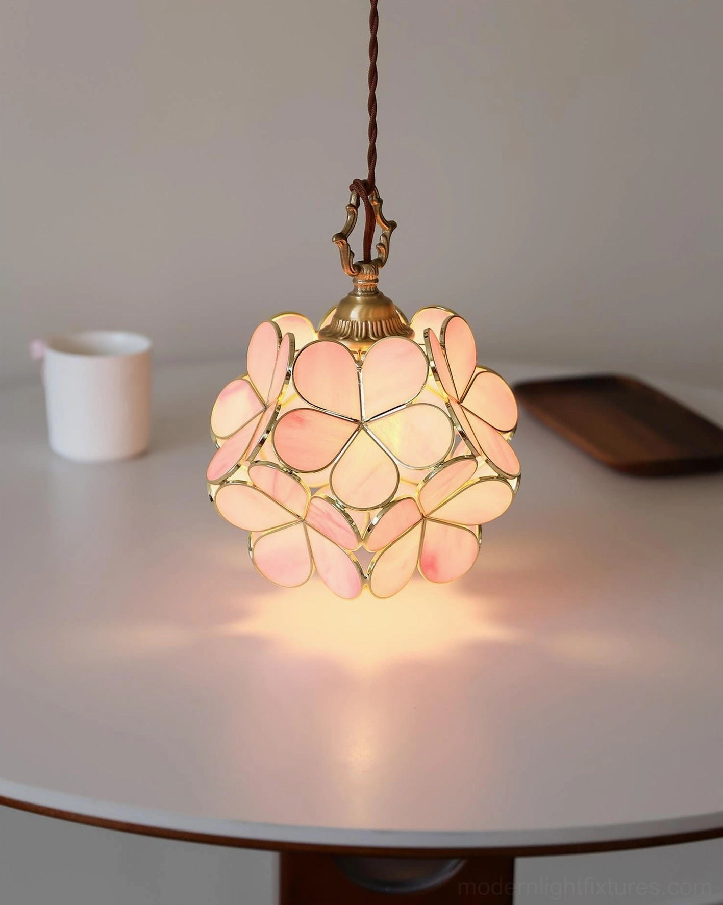 Lit pink and brass floral pendant light suspended above round dining table setting