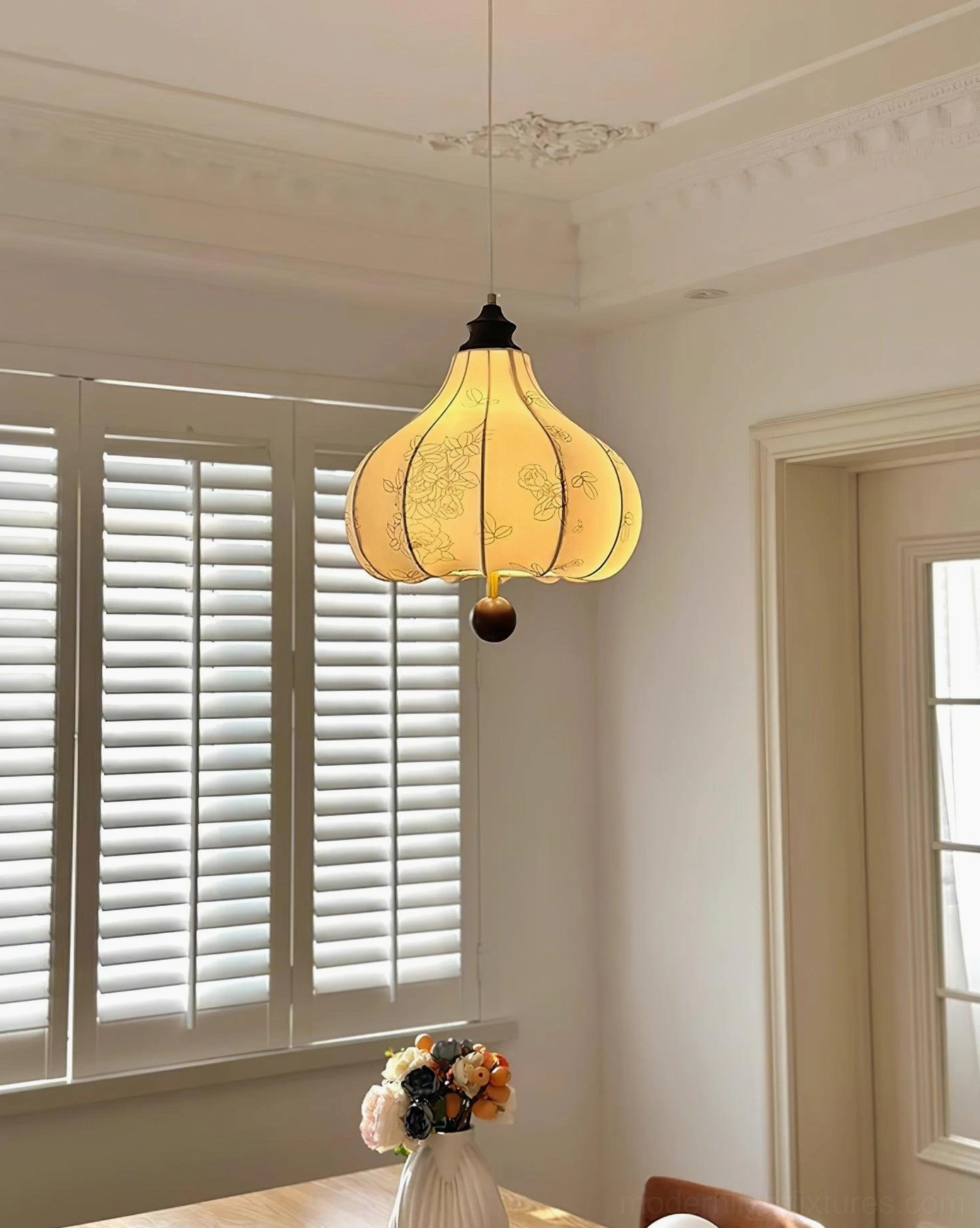 Fabric lantern pendant light in vintage dining room with louvered windows, warm yellow-toned shade creating elegant ambiance