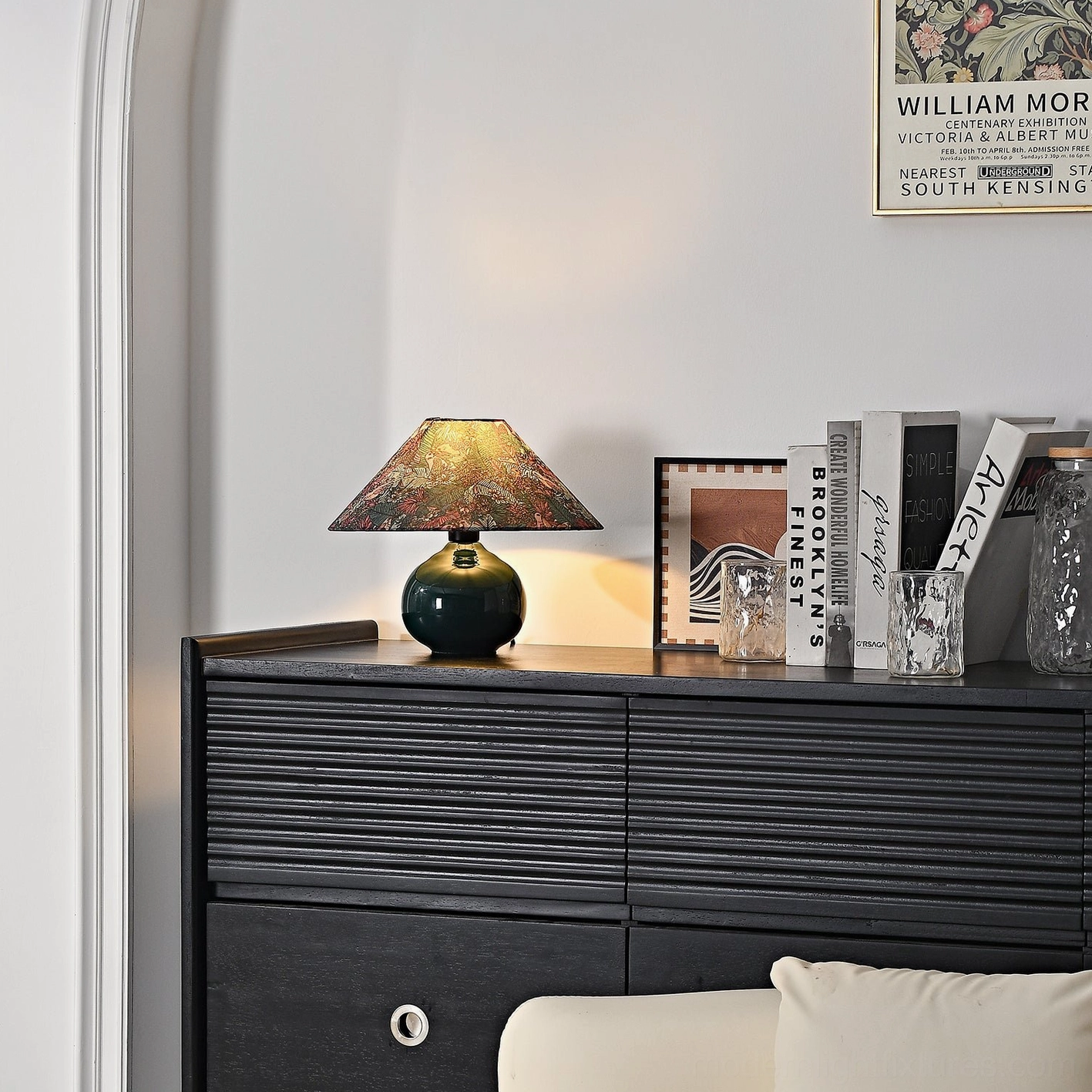 Modern botanical ceramic lamp on living room console table with stacked books and glassware in sophisticated interior design arrangement