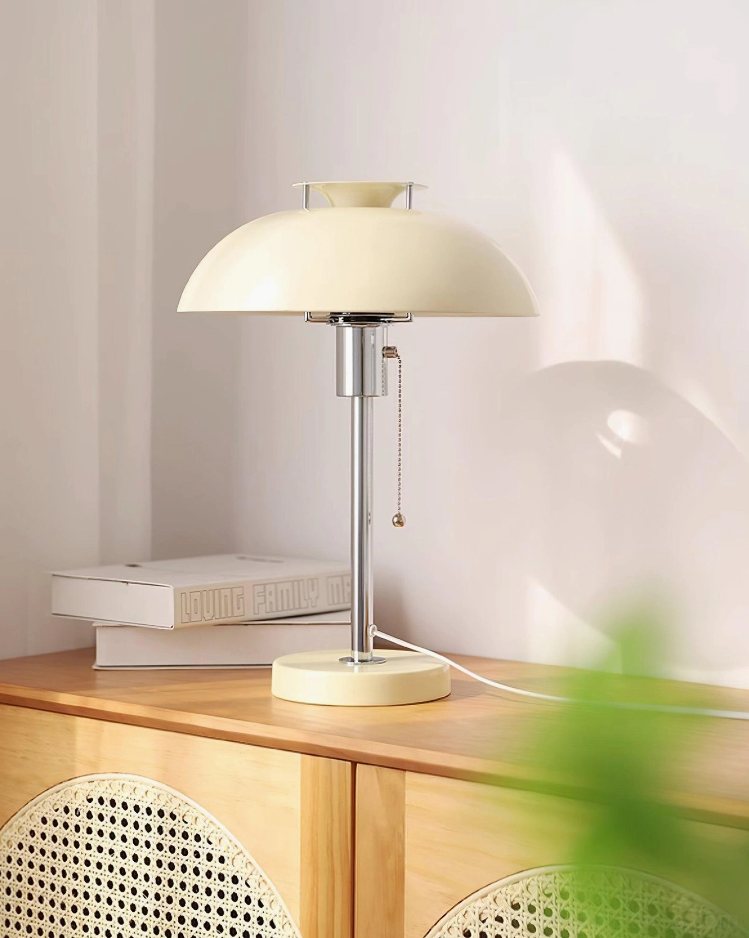 Cream white beige Bowie table lamp on rattan wooden cabinet with stacked books, minimalist retro design