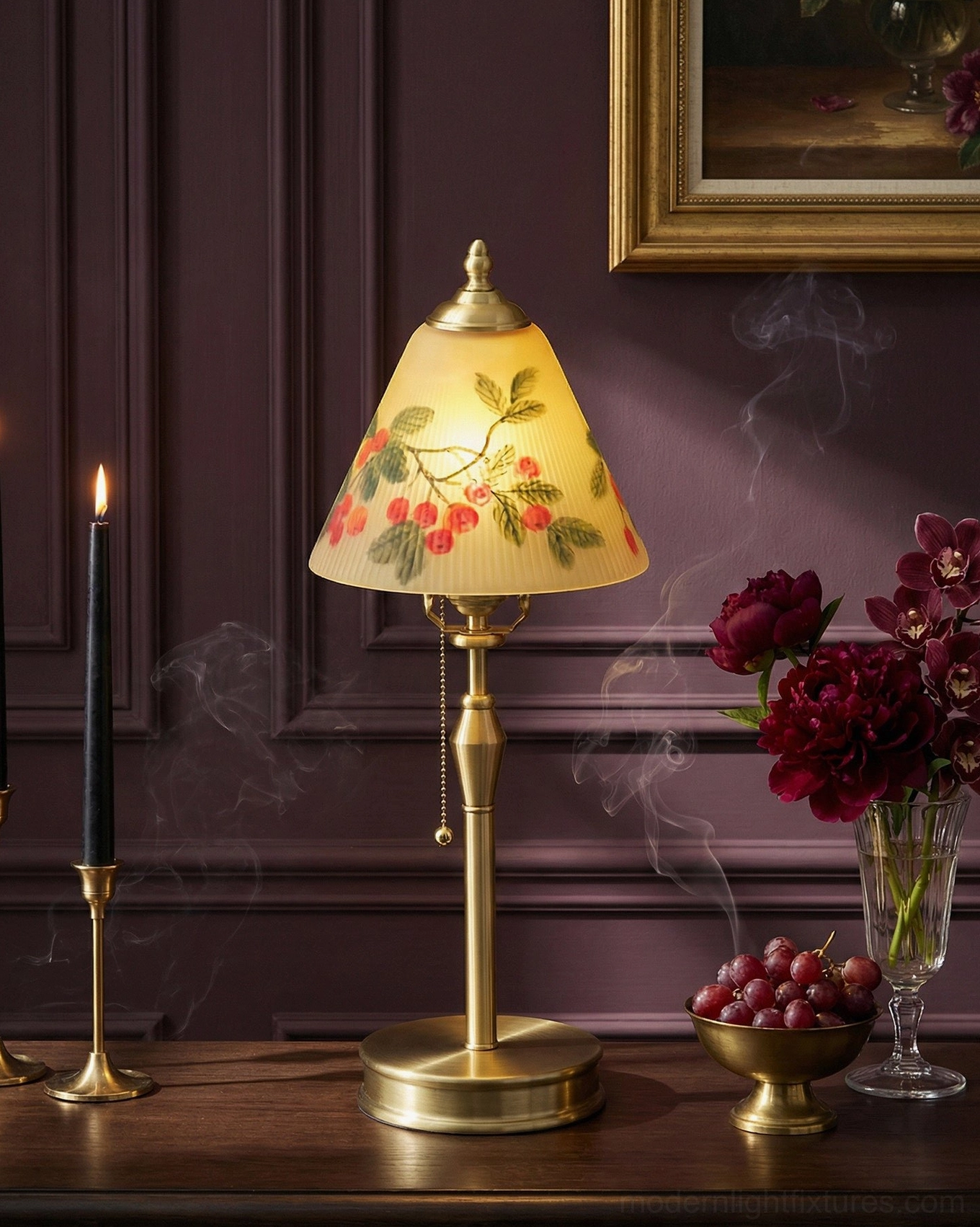 Lit Bramelle table lamp glowing warm on dark burgundy wall with wooden console, showing soft ambient light through hand-painted glass