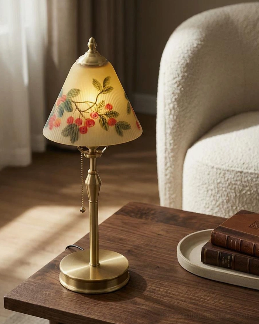 Bramelle hand-painted brass table lamp lit on living room side table with fluffy sofa and stacked books, warm ambient lighting