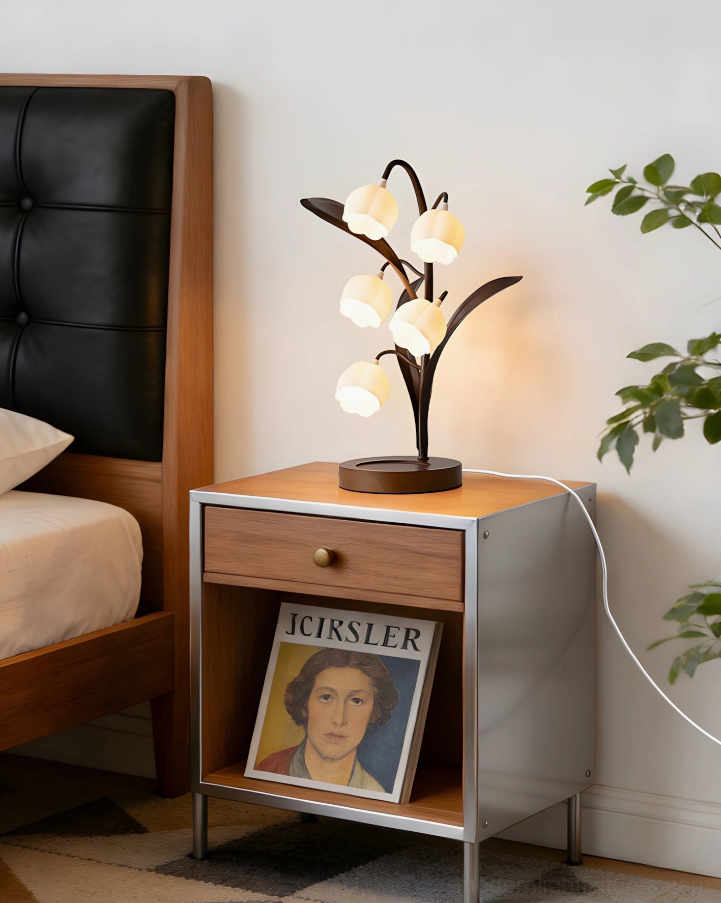 Modern botanical lamp on bedside table beside leather bed with visible power cord in bedroom interior