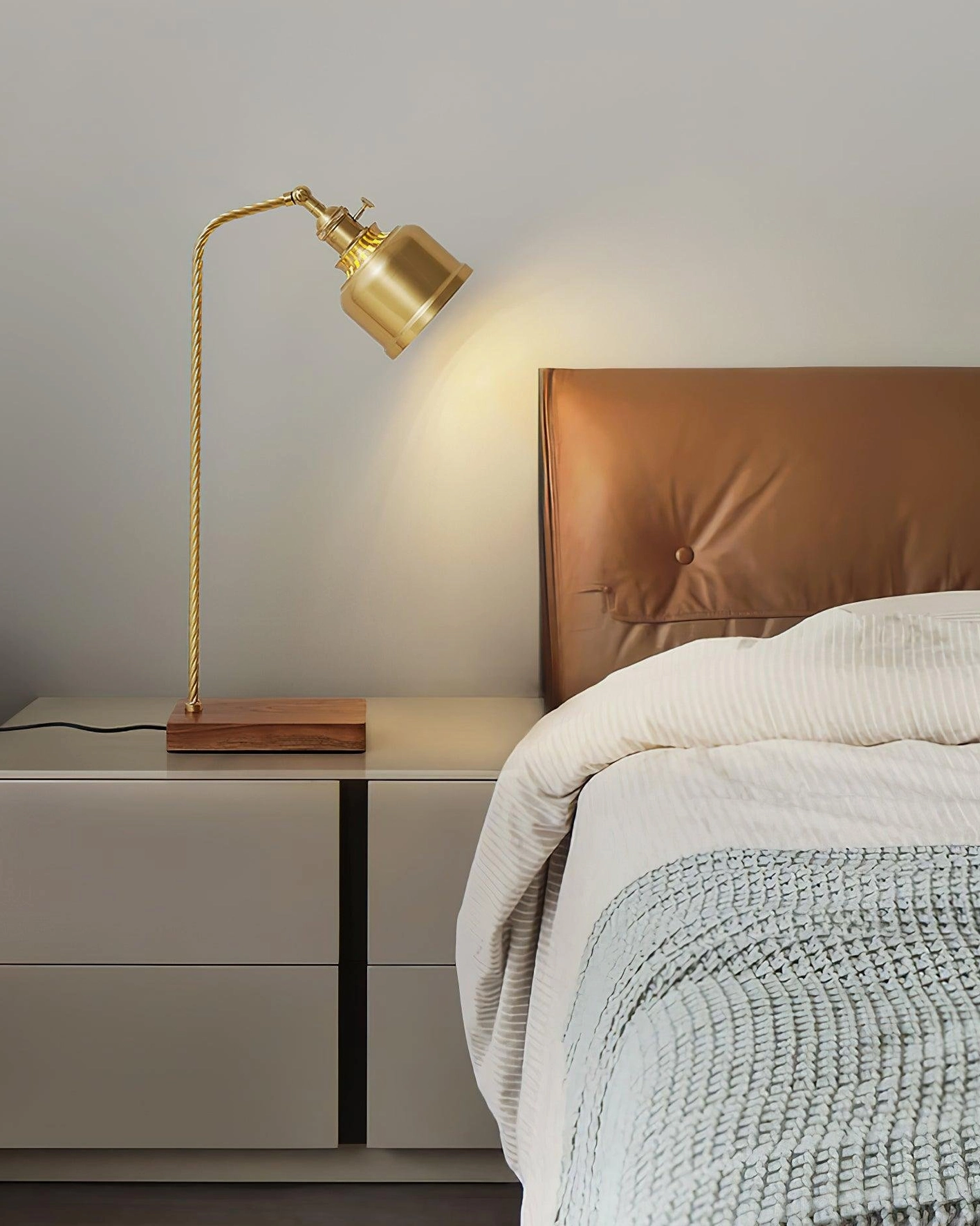 Brass nightstand lamp in modern bedroom with brown leather headboard and warm wall lighting