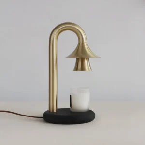 Brass and black wood base candle warmer lamp with lit white scented candle on gray tabletop