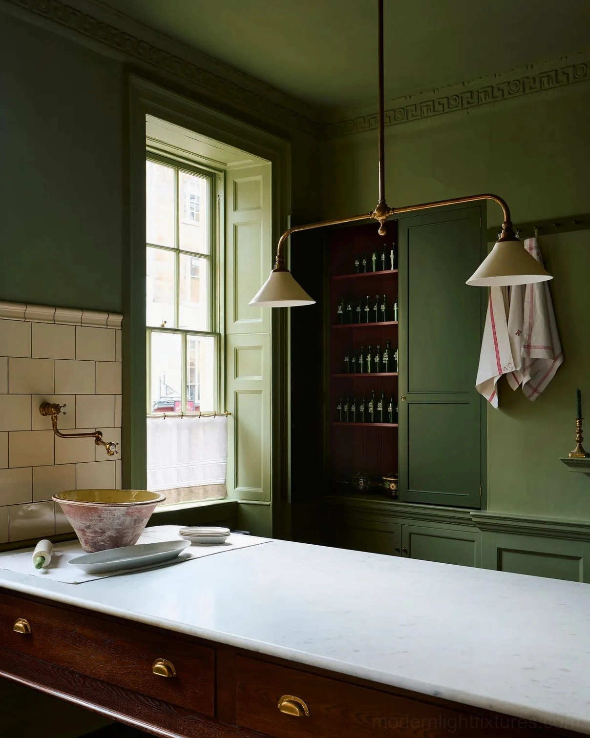 Two-light brass linear pendant lamp with off-white conical shades displayed in sage green tiled vintage kitchen setting