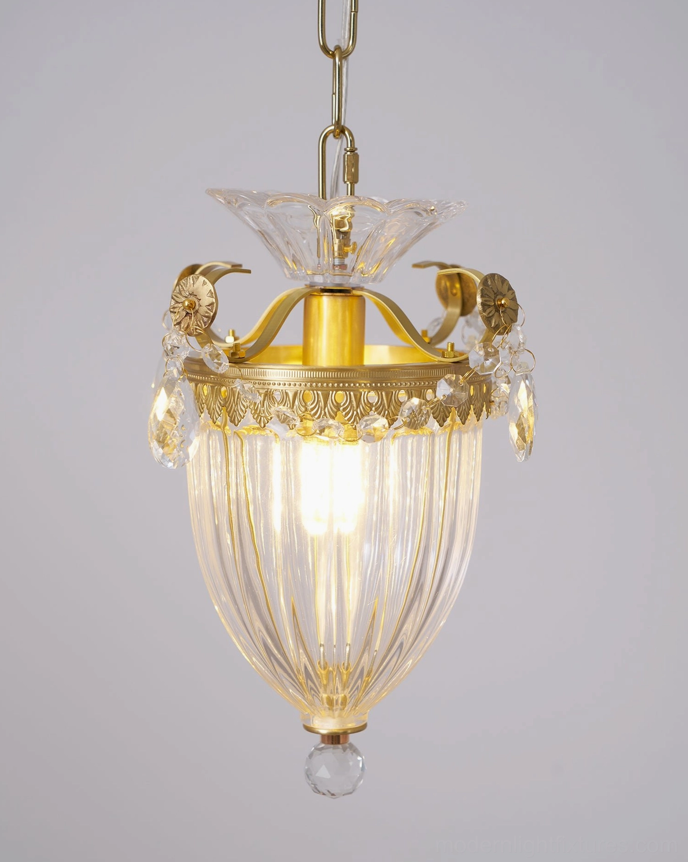 Lit crystal pendant chandelier with low-angle view highlighting brass details and hanging crystals