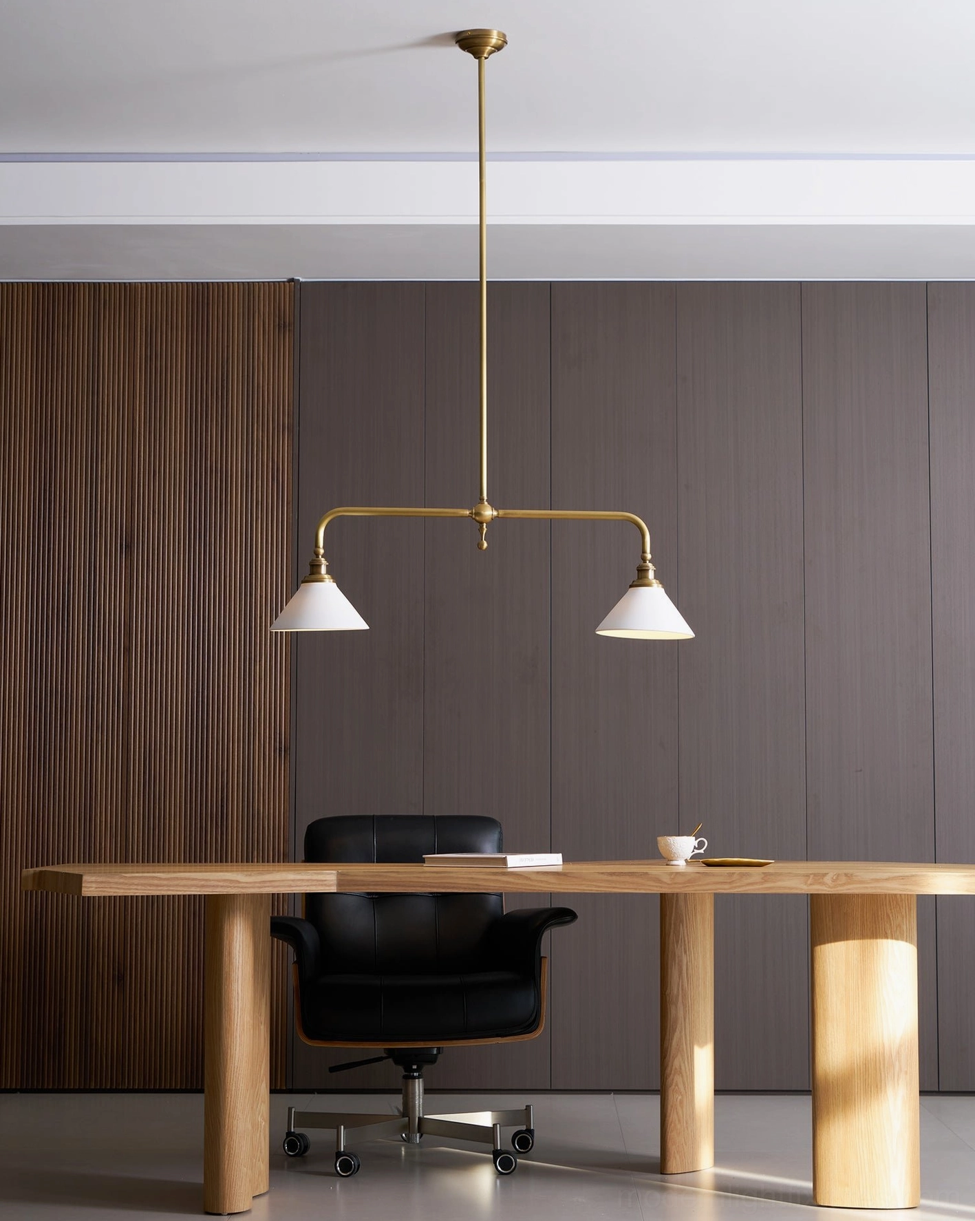 Two-light linear pendant chandelier with aged brass finish and white ceramic shades in modern home office workspace
