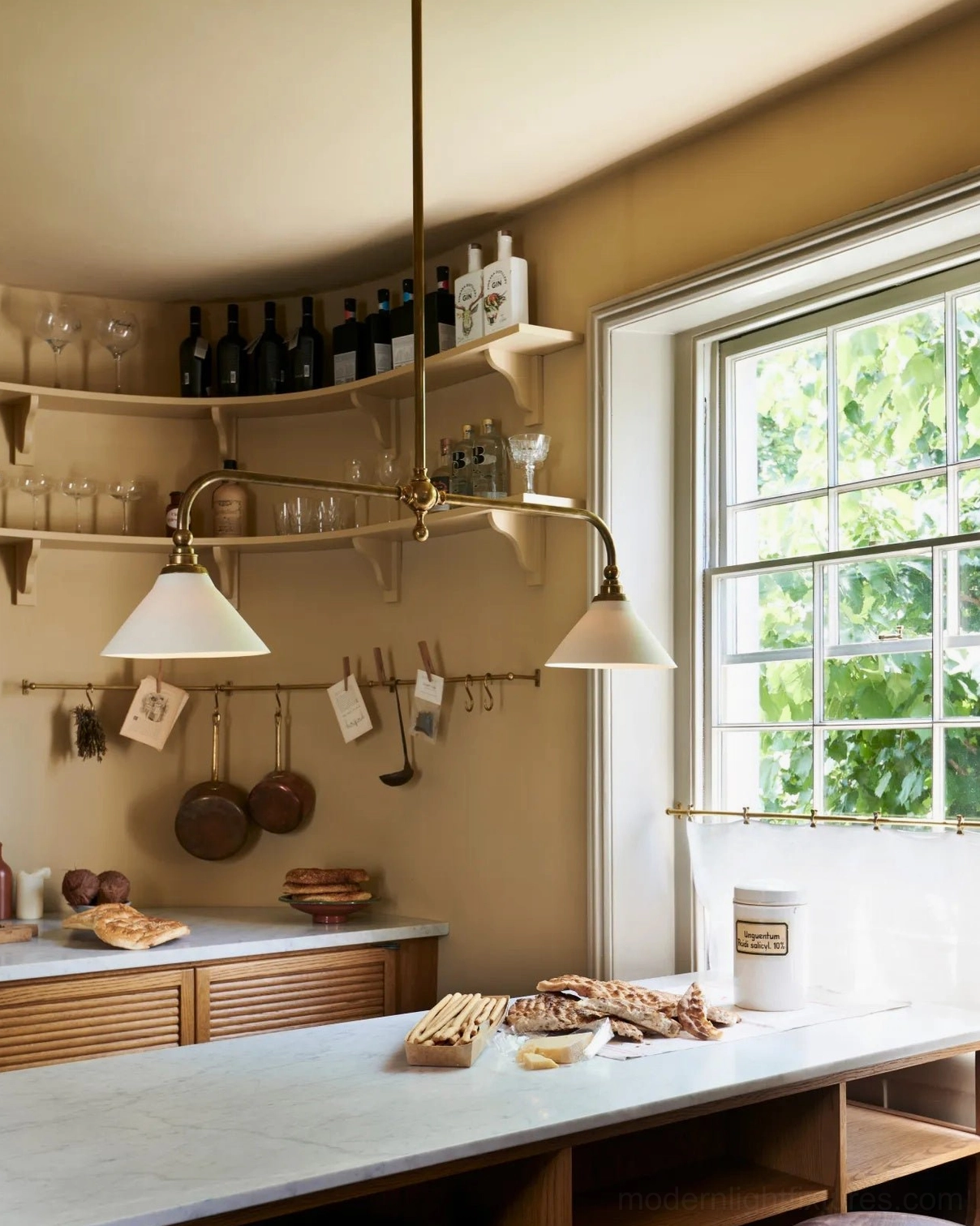 Aged brass linear chandelier with white conical shades demonstrating warm ambient lighting in residential interior