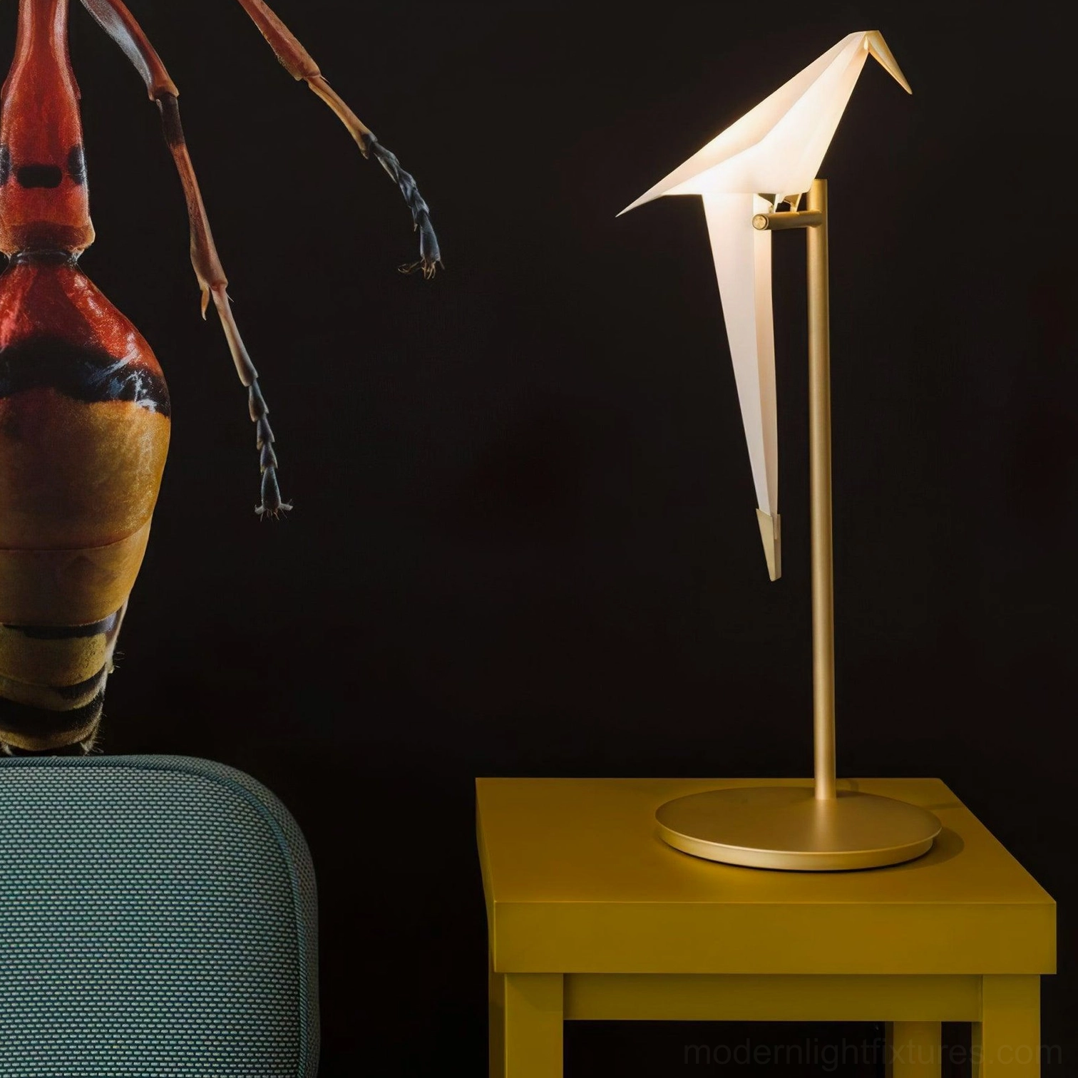 Warm glowing origami crane table lamp on yellow accent table with insect artwork backdrop luxury design