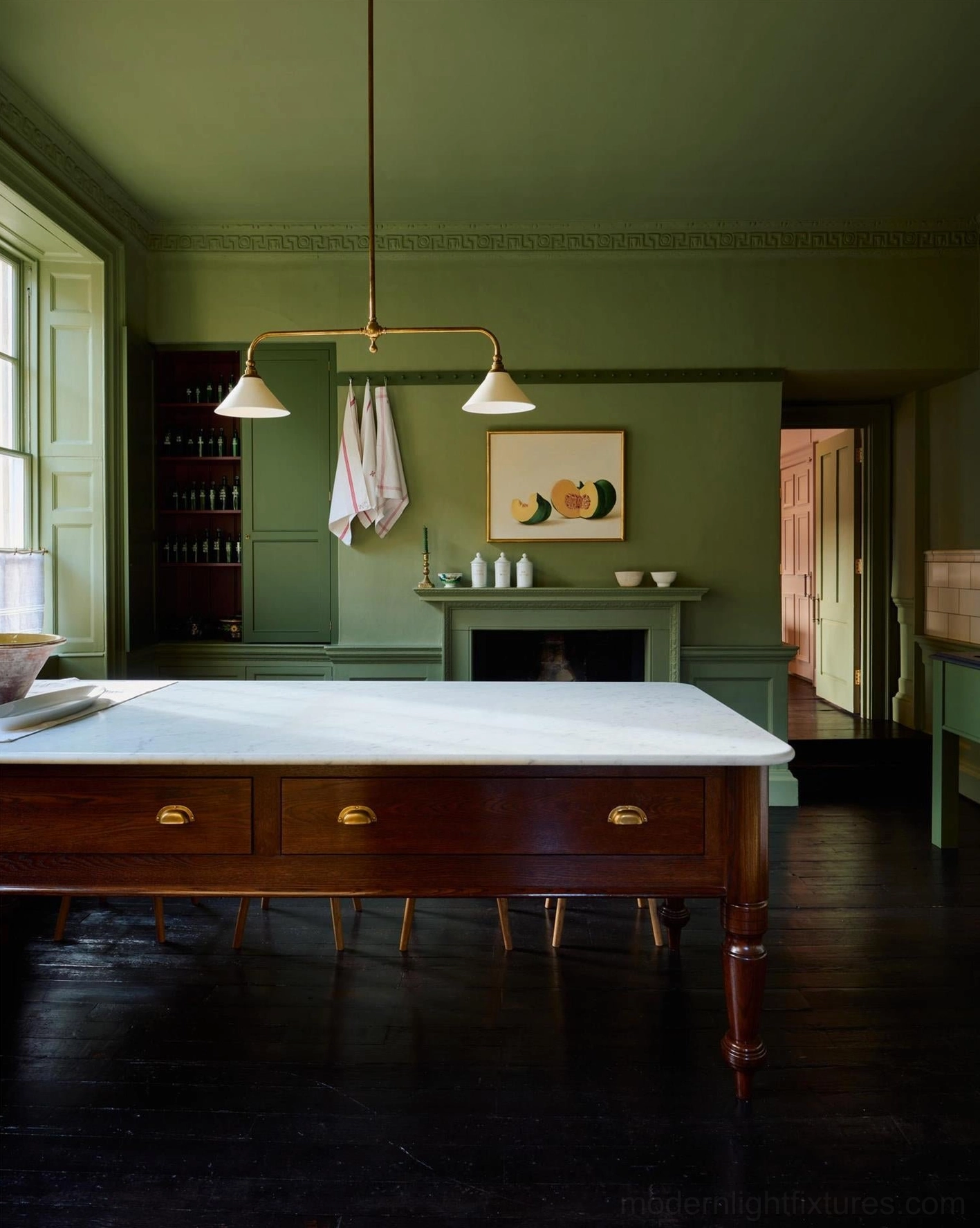 Brass linear chandelier installed above dark green vintage kitchen island, classic country house interior design with warm lighting