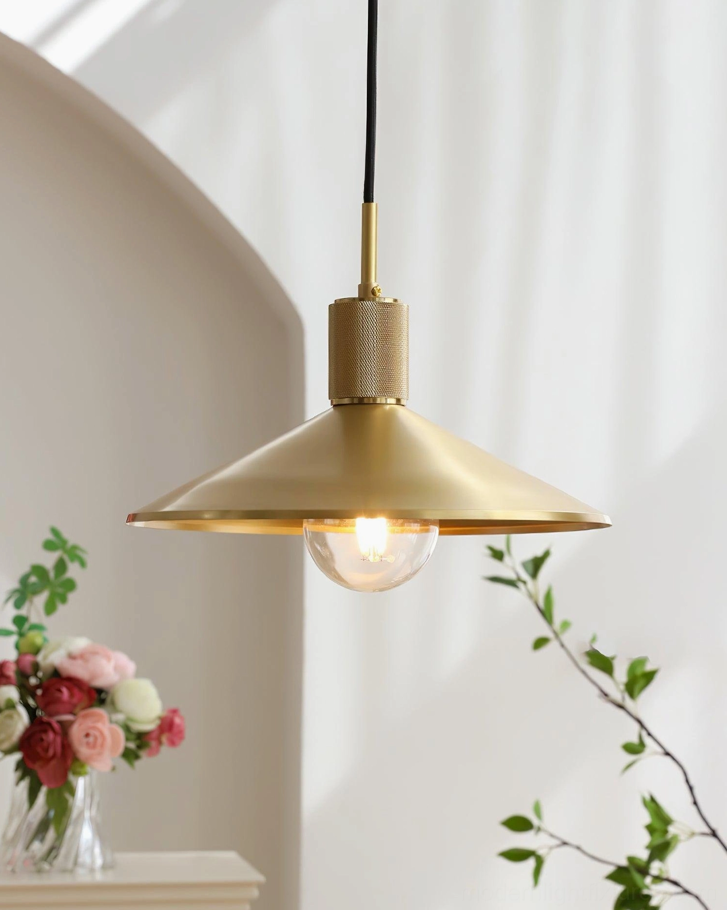Brass pendant light with illuminated exposed vintage bulb in low angle front shot against archway background