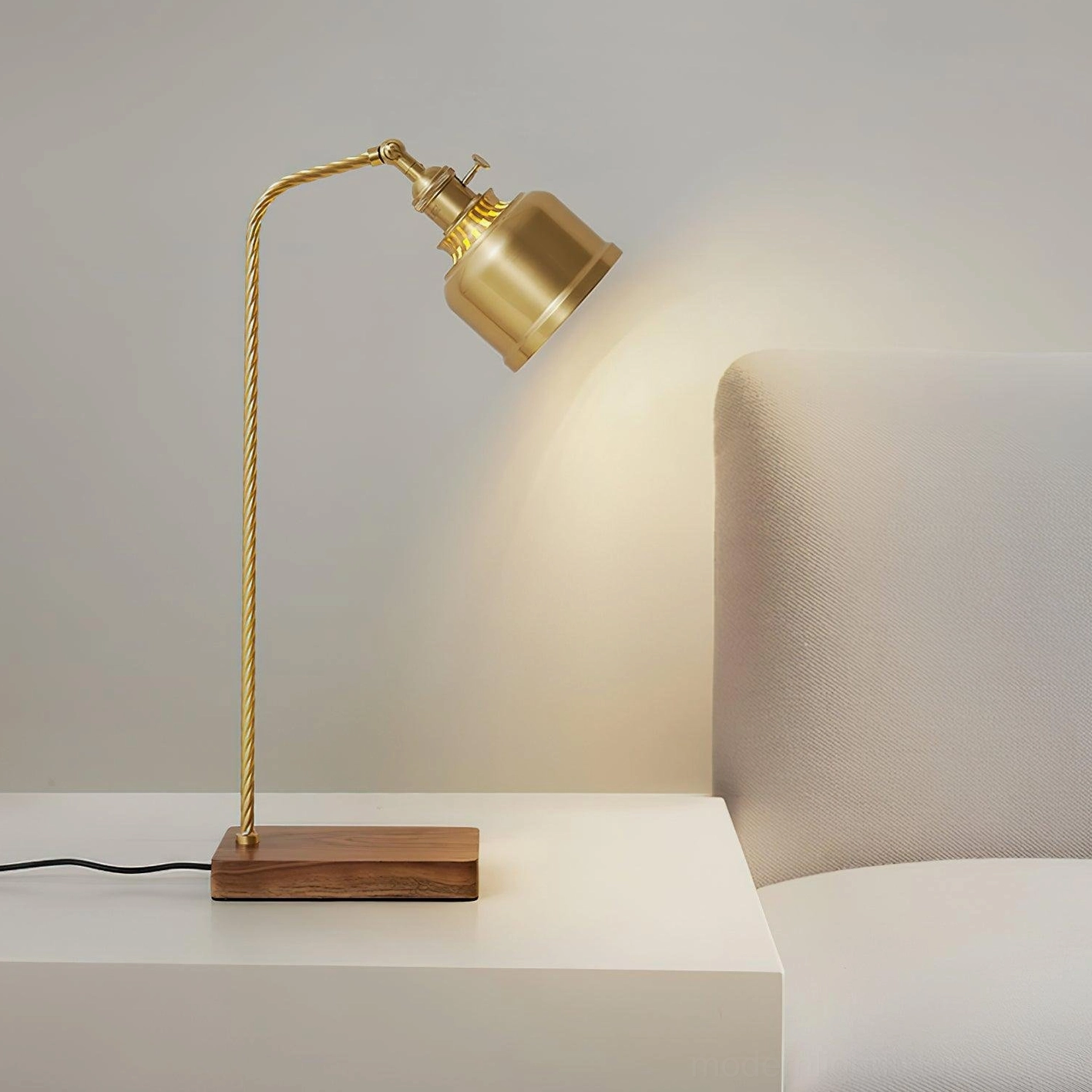 Industrial brass table lamp with adjustable shade on minimalist white side table near fabric chair