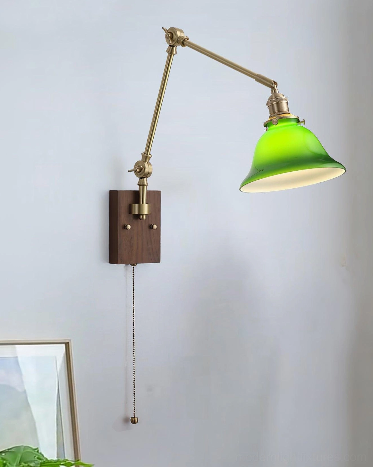 Vintage brass swing arm wall sconce with green glass shade mounted on walnut base, front angled view with framed artwork display