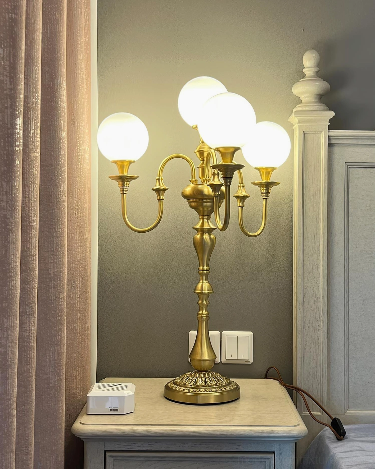 Neoclassical brass candlestick table lamp positioned on bedroom nightstand next to bed