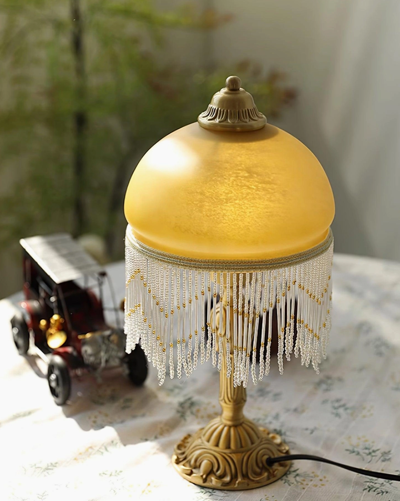 Vintage brass table lamp left angle with green plant backdrop creating natural warm home vibe and cozy atmosphere