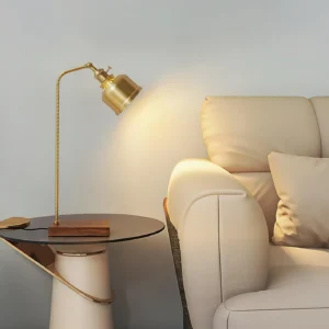 Brass table lamp in living room setting next to beige fabric sofa, warm ambient lighting with matte gold finish