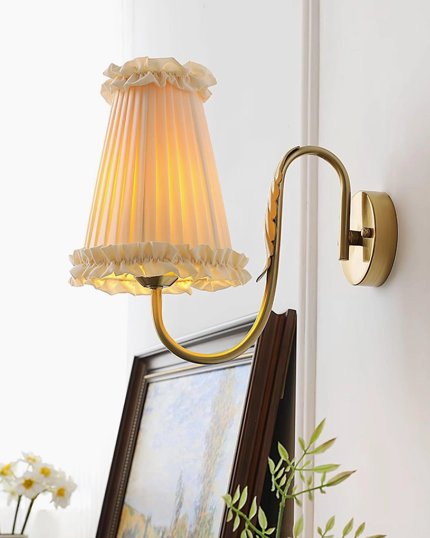 Brass wall sconce with illuminated pleated shade in modern home interior setting