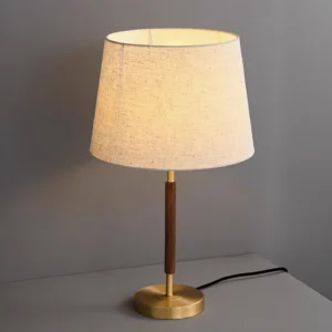 Lit mid-century modern table lamp with warm glow, brass base and walnut pole, front three-quarter view
