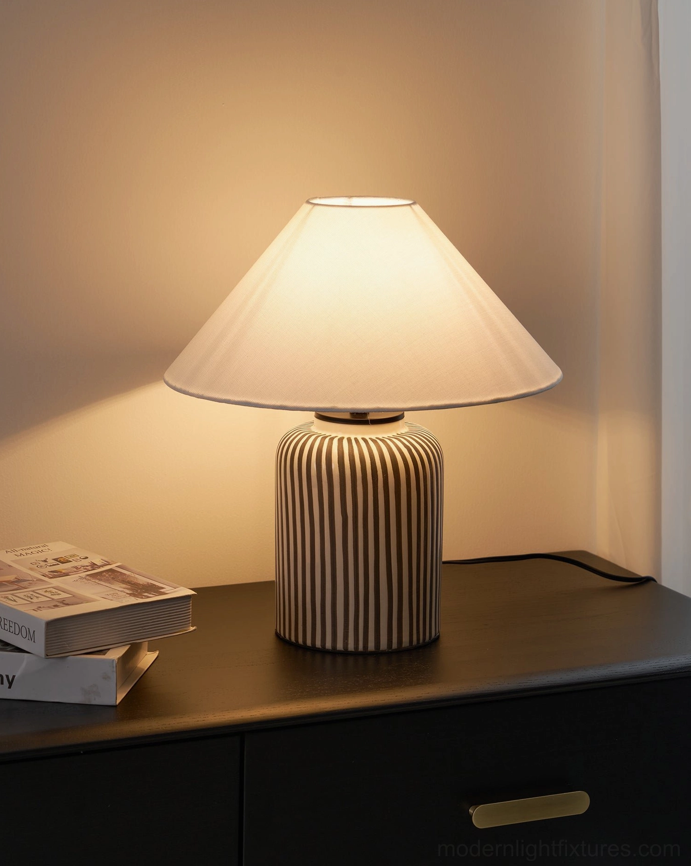 Striped ceramic table lamp on dark wood nightstand with gold drawer pulls and stacked books beside