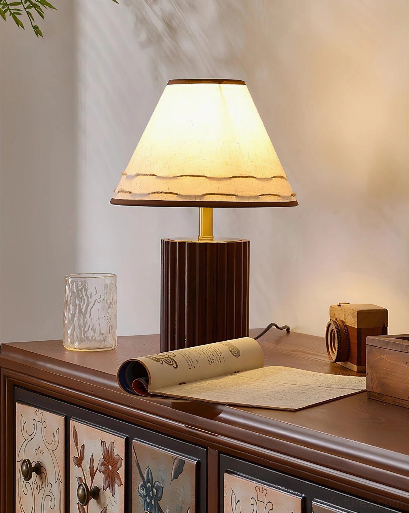 Wooden desk lamp with dark walnut base positioned on retro painted dresser with rolled book and vintage camera styling