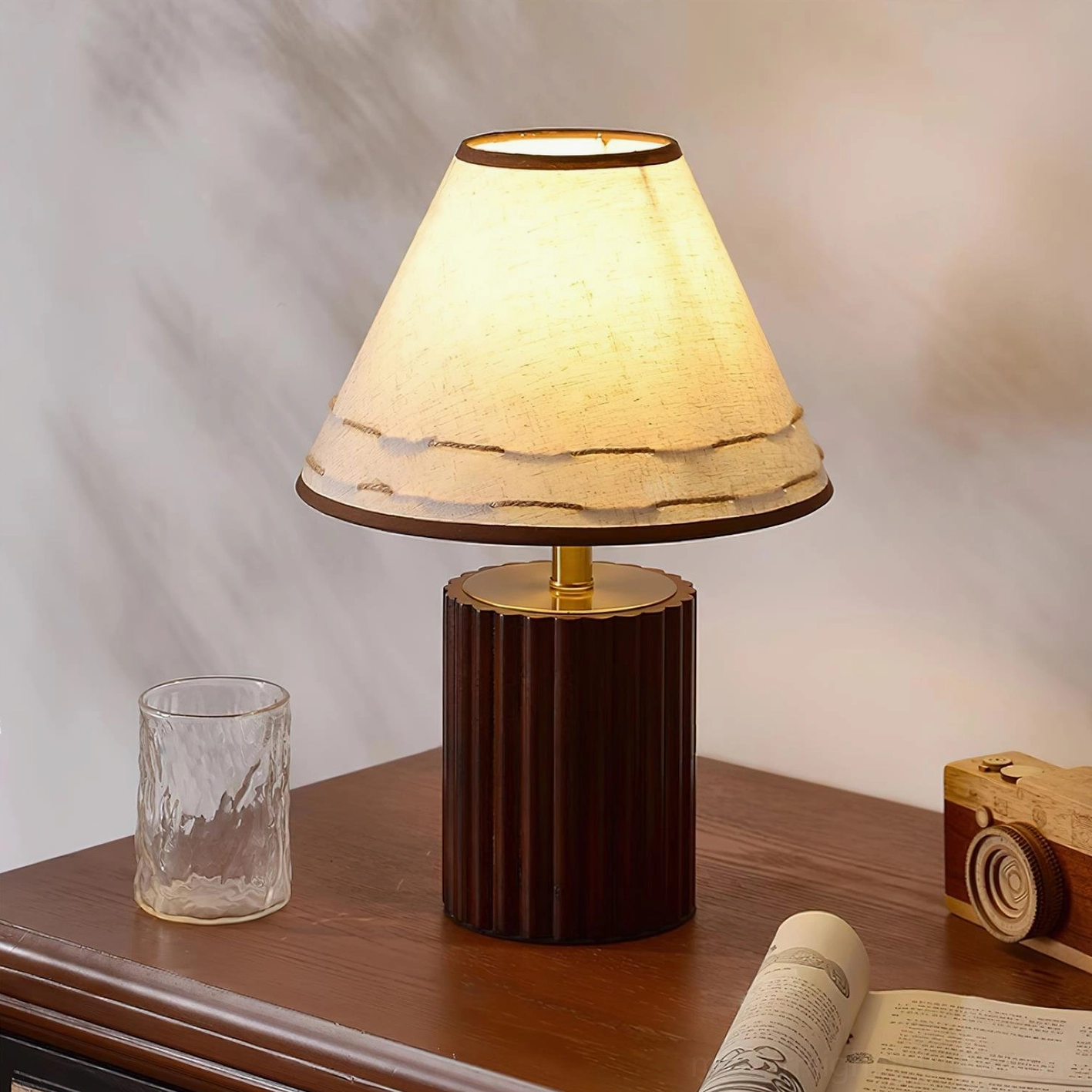 Handmade wooden table lamp with walnut base providing warm ambient light on wooden surface with book and vintage camera