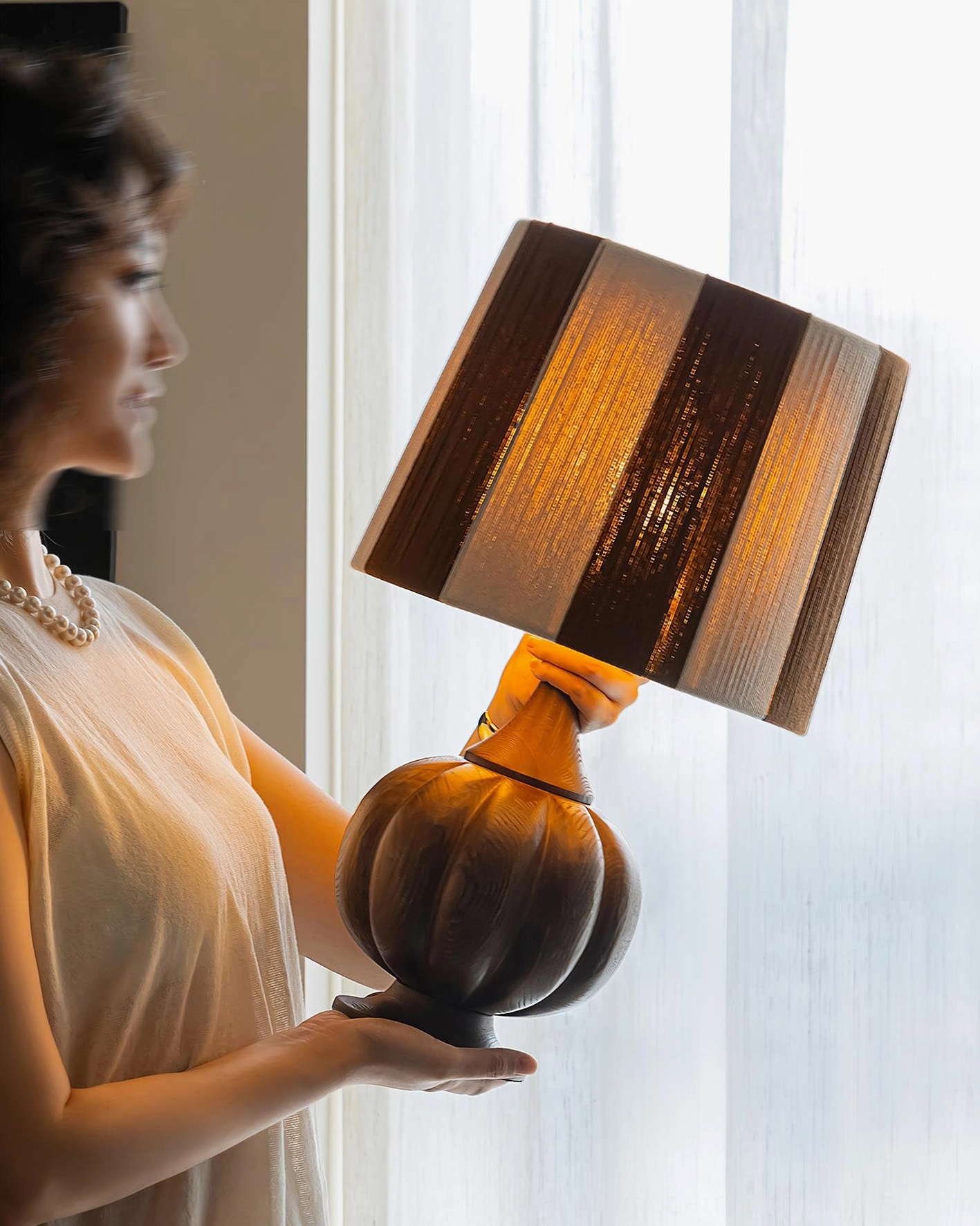 Wooden pumpkin base striped table lamp with brown-toned shade, side view held by person in bright interior