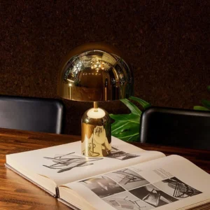Gold modern table lamp displayed on wooden dining table beside coffee table books with warm ambient lighting