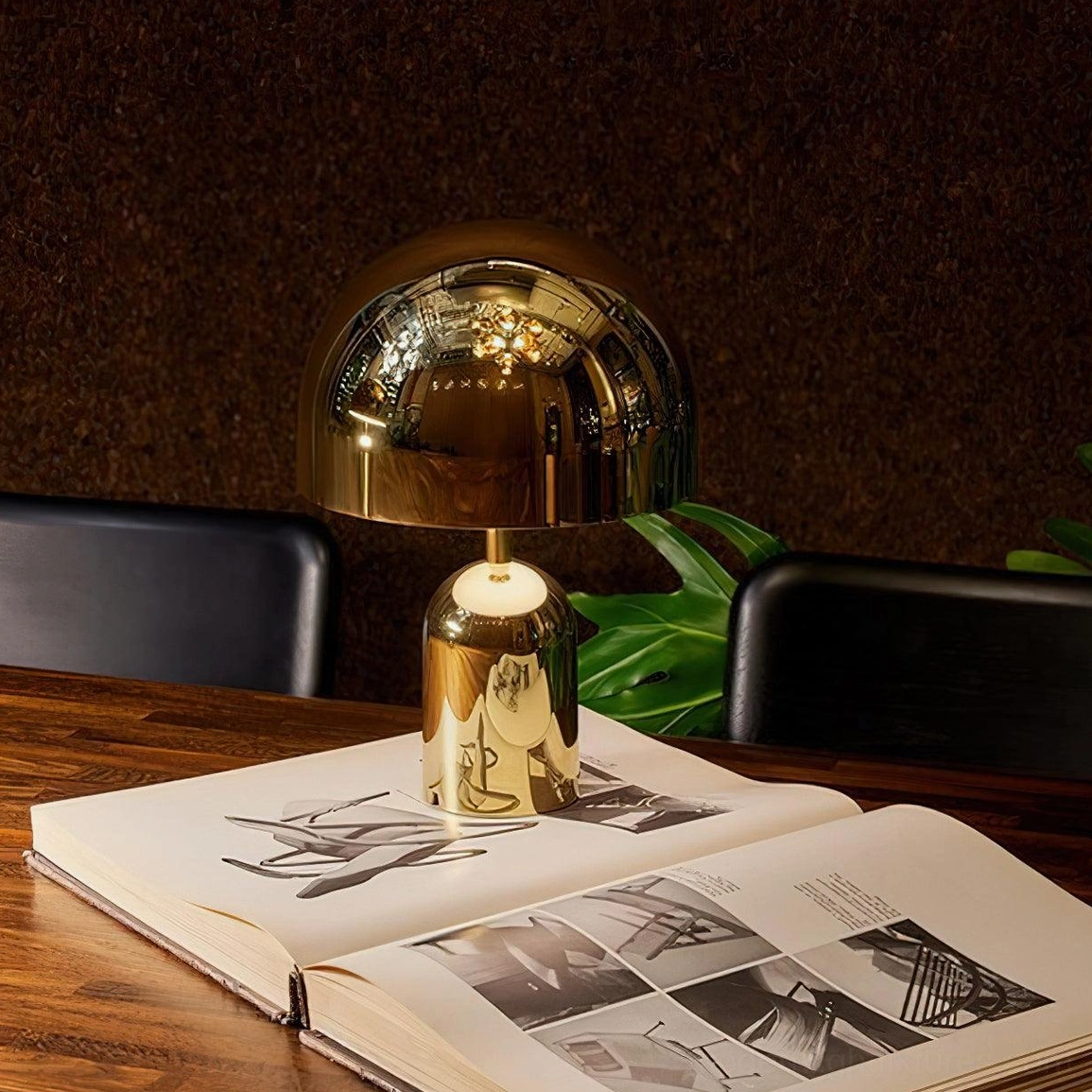 Gold modern table lamp displayed on wooden dining table beside coffee table books with warm ambient lighting