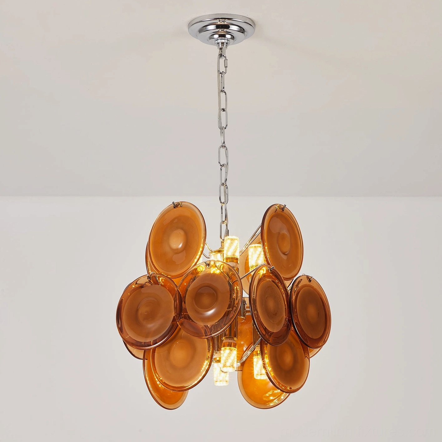 Illuminated amber glass disc pendant chandelier three-quarter view, showcasing interior light diffusion through translucent glass
